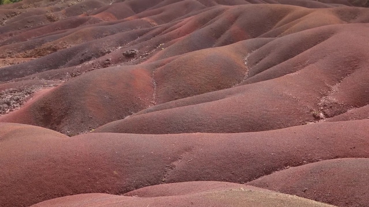 Close-up aerial view of the unique undulating dunes of the Seven Coloured Earth in Chamarel, Mauritius, showcasing the distinct layers of vibrant, multicolored volcanic mineral sand