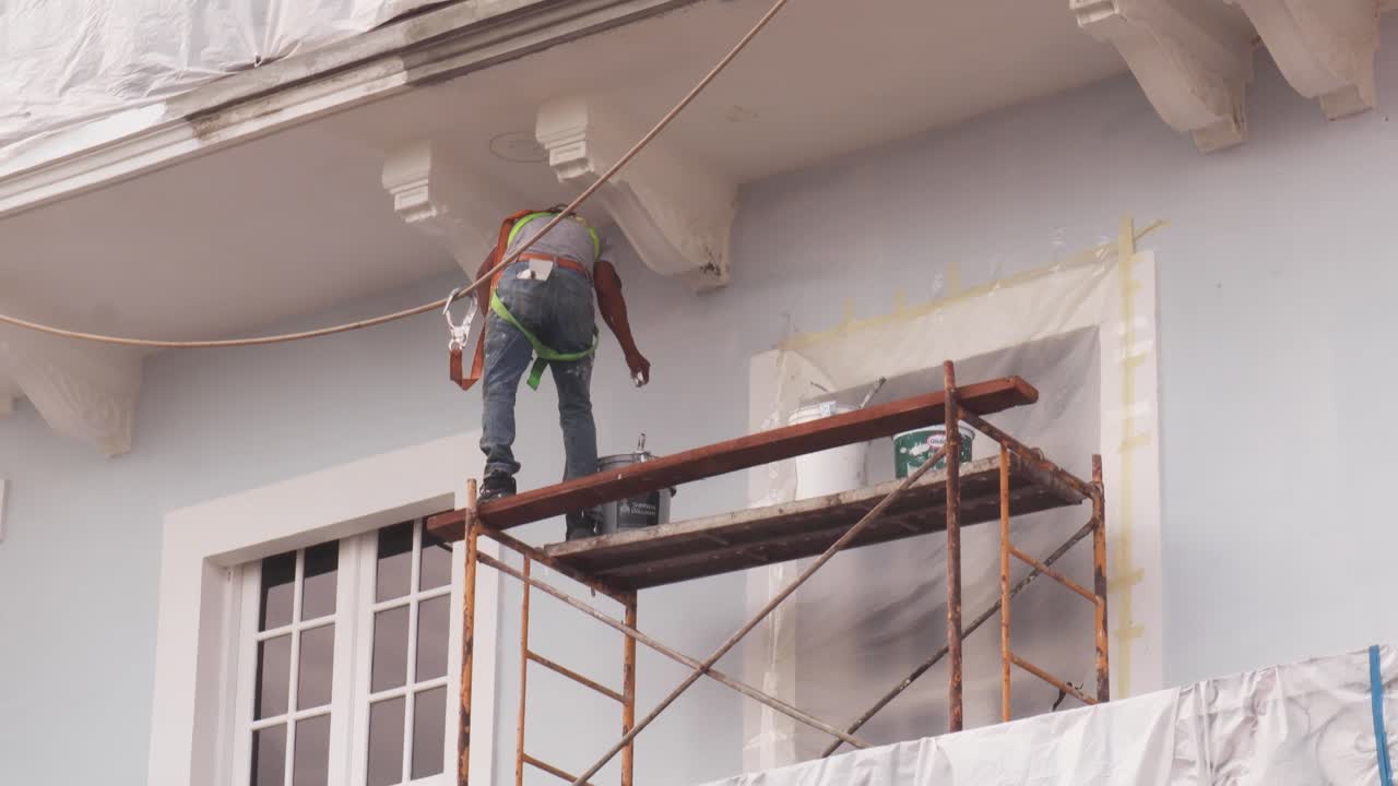 trabajador profesional parado sobre un andamio con un balde pintando el exterior de un hermoso edificio con arquitectura hispana durante un caluroso día soleado de verano en el casco viejo de la ciudad de panamá