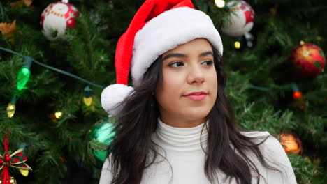 una mujer hermosa con un sombrero de santa claus bailando y celebrando la temporada navideña con un árbol de navidad decorado y adornos