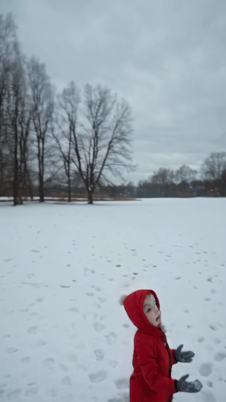 A child in a red coat stands in a snowy field, captured from a low angle