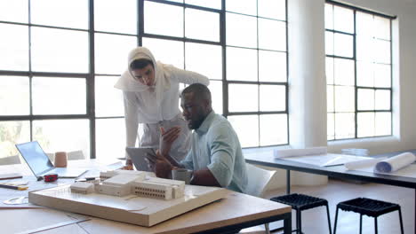 reviewing architectural model and tablet, colleagues discussing project details in office