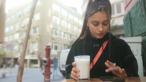 joven disfrutando de una bebida y usando el teléfono en un café