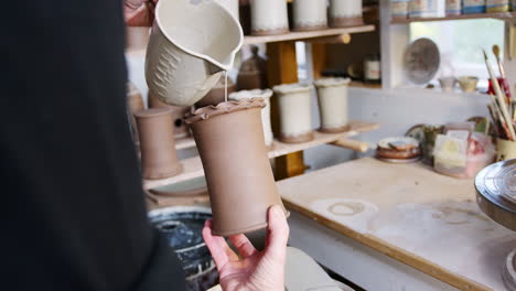 close up of male potter applying glaze to clay vase in ceramics studio