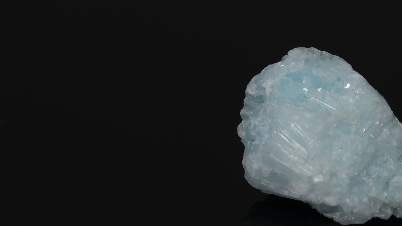 A detailed view of a blue mineral fragment rotating against a dark background, showcasing its texture and color.