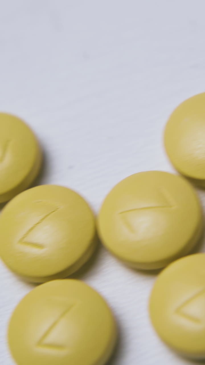 small heap of bright yellow pills with marks lies on clean light background extreme close view