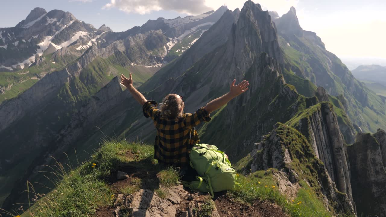Slow motion: Young man on a hike contemplates stunning mountain range view. Arms wide open