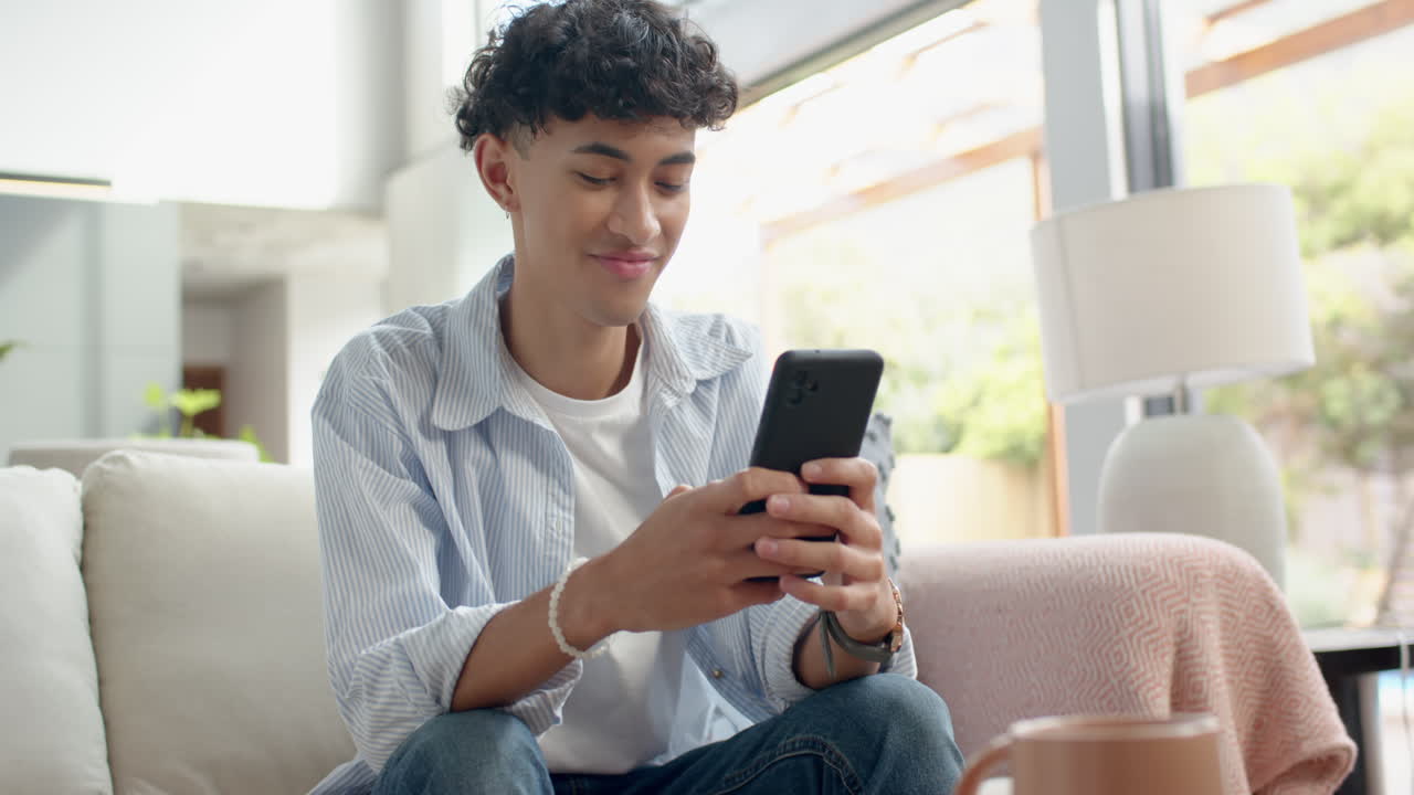 Using smartphone, teenage boy sitting on couch and smiling at home