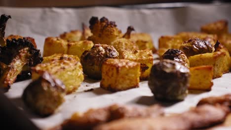 a close up shot panning across a baking tray revealing an assortment of vegetables on a layer of greaseproof paper roasting in a hot oven