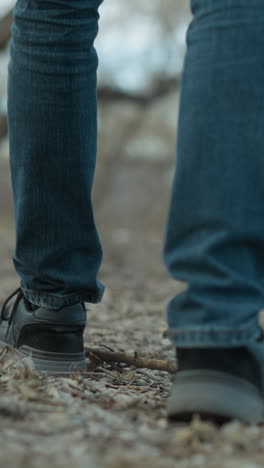 toma de primer plano de una persona de pie en un camino del bosque, con zapatillas negras y vaqueros azules, el suelo está cubierto de hojas y ramas