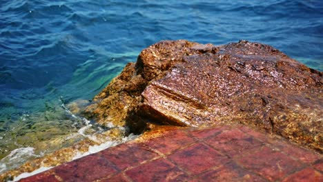 El-Agua-Rompiéndose-Y-Estrellándose-Sobre-Rocas-Y-Ladrillos-En-La-Casa-Del-Mundo,-Lago-Atitlán,-Guatemala