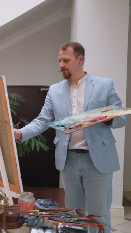 una mujer se sienta tranquilamente posando para un artista masculino en el estudio. un pintor profesional crea un retrato de una modelo atractiva de pie junto al caballete. rutinaria del taller de arte