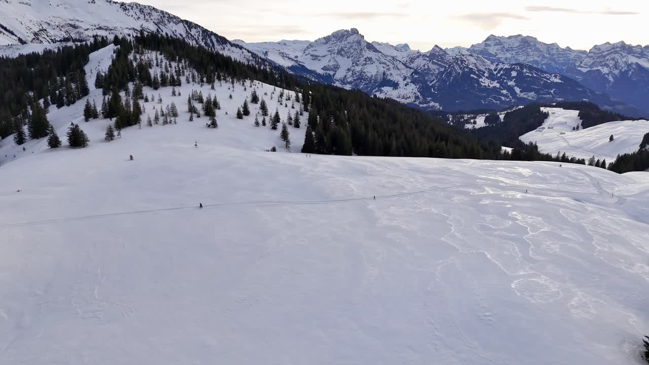Vast snowy landscape in Switzerland with distant skiers and mountain backdrop, aerial view
