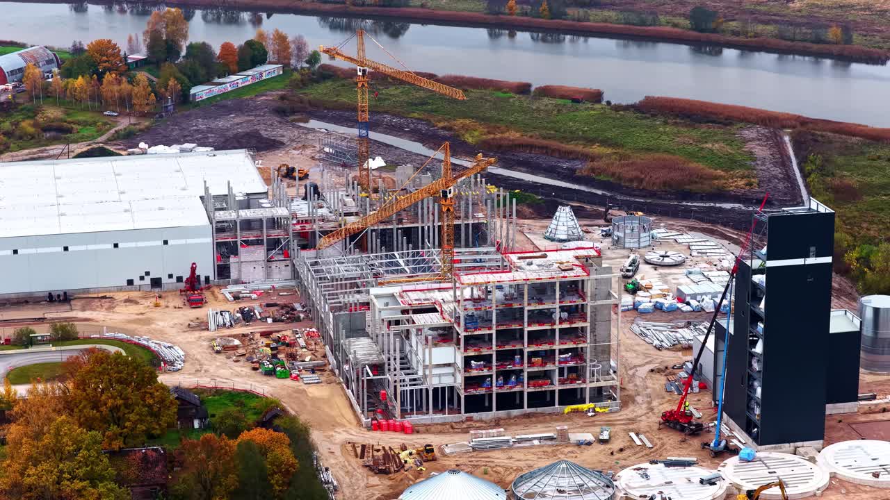 An Industrial Complex is Being Built With Cranes Above a Multi-story Steel Structure - Orbit Drone Shot
