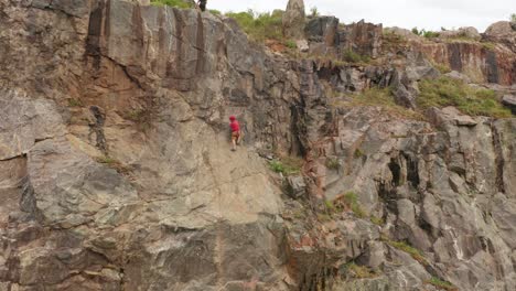 a man wearing a red helmet and a red vest is climbing the mountain, while a woman is waiting for him at the peak