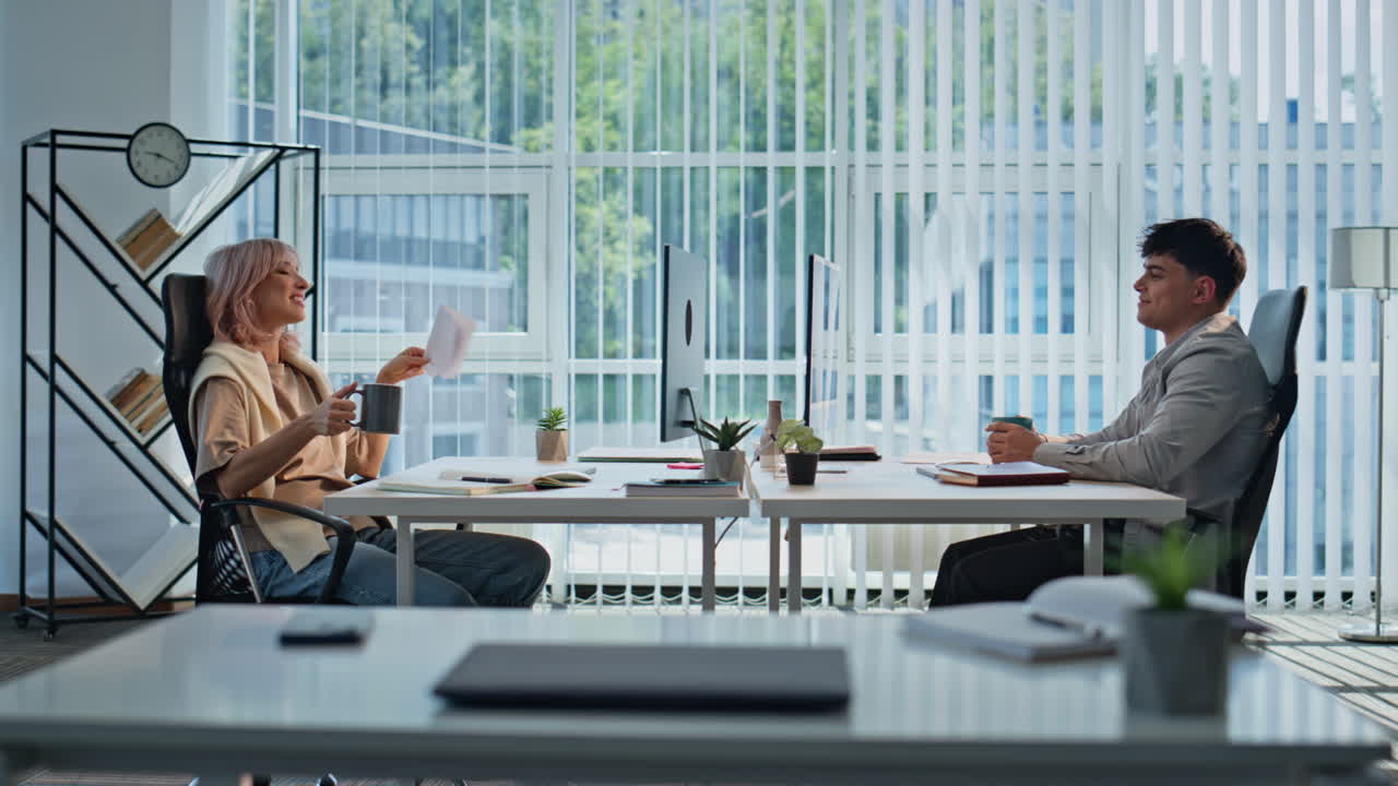 Woman holding cup talking colleague at panoramic office. Coworkers enjoying brea