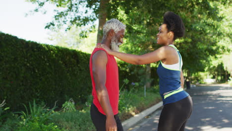 una pareja de ancianos afroamericanos sonrientes haciendo ejercicio al aire libre estirándose en la carretera