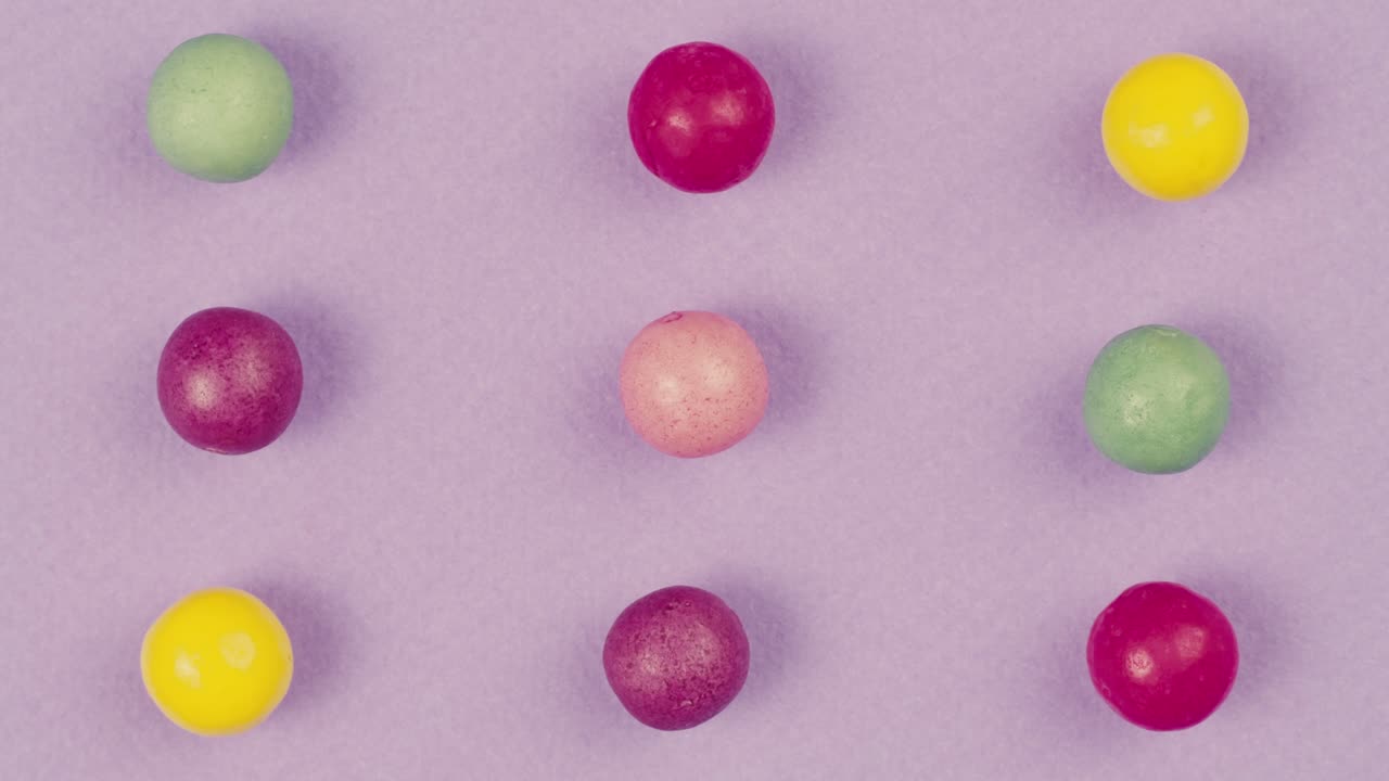 Colorful dragee candies on purple background. Summer bright texture studio shot for store, supermarket, close-up top view, zoom. Children's sweets made of sugar, mix of lollipops.