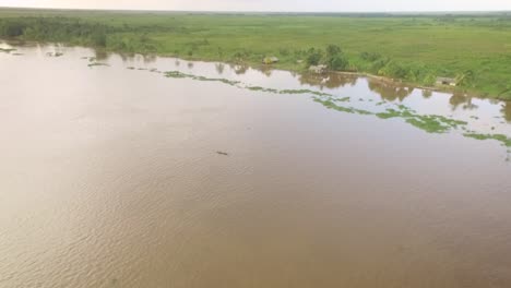 vista aérea de una pequeña canoa indígena que navega por el río orinoco con pequeñas casas indígenas en la orilla