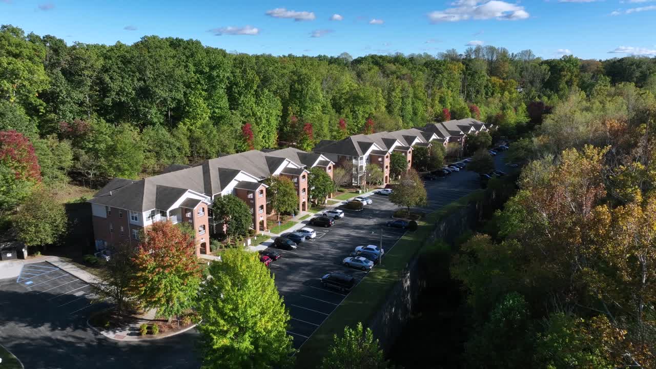 Aerial approaching shot of american multi family units between forest trees on sunny day in fall season. Quiet suburb neighborhood of America with parking cars. Wide shot