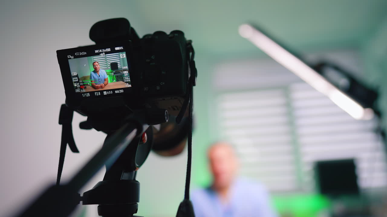 Vista laterale di una telecamera che riprende un medico in clinica. Vista laterale di telecamera e treppiede che riprendono un medico in una sala clinica con luce LED e sfondo verde
