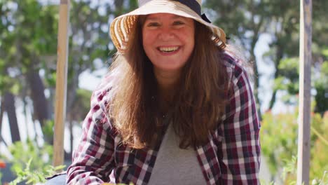 portrait of happy caucasian woman wearing hat, gardening and smiling in garden