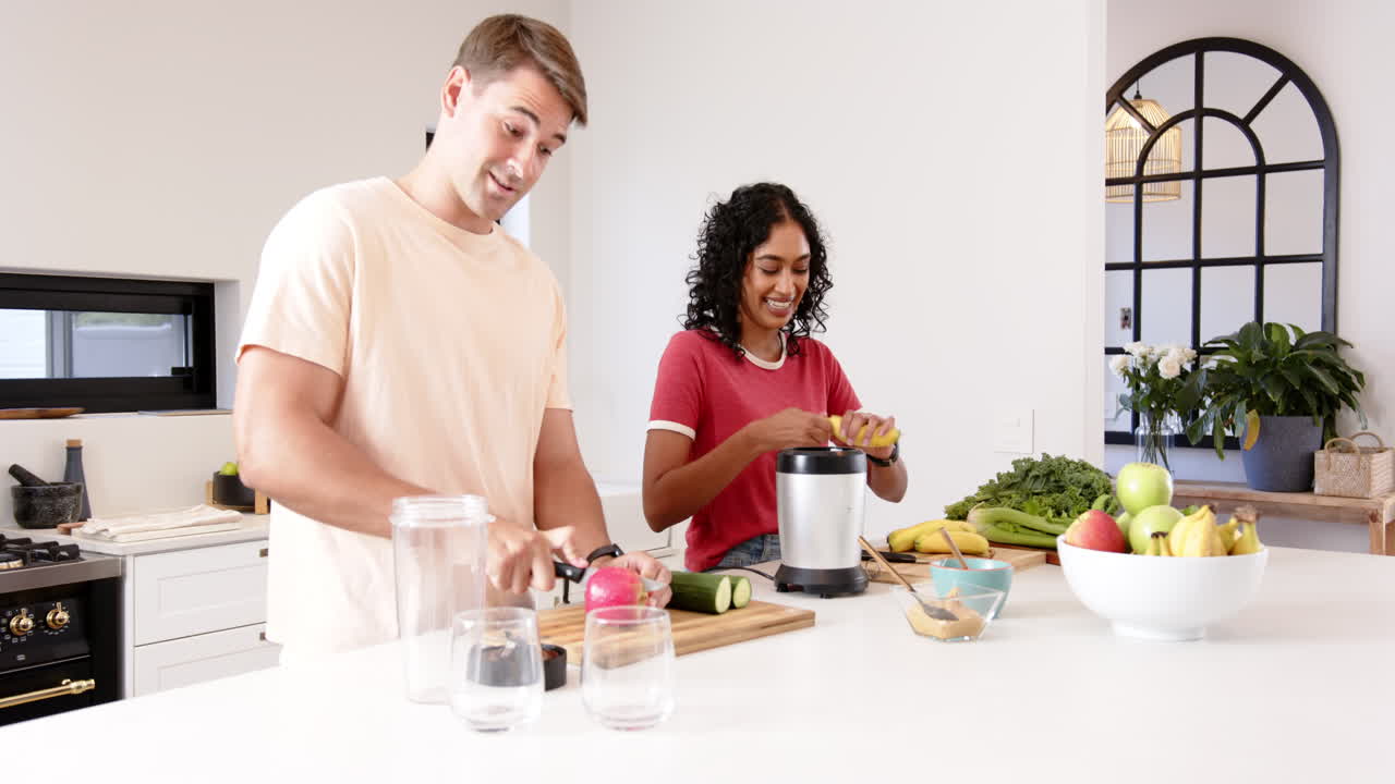 Preparing fresh smoothie, young multiracial couple cutting fruits and vegetables in kitchen, at home