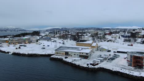 Vista-De-Drones-En-Tromso-De-Finnsnes,-Un-Pequeño-Pueblo-Lleno-De-Nieve-Y-Montañas-En-El-Horizonte-En-Noruega