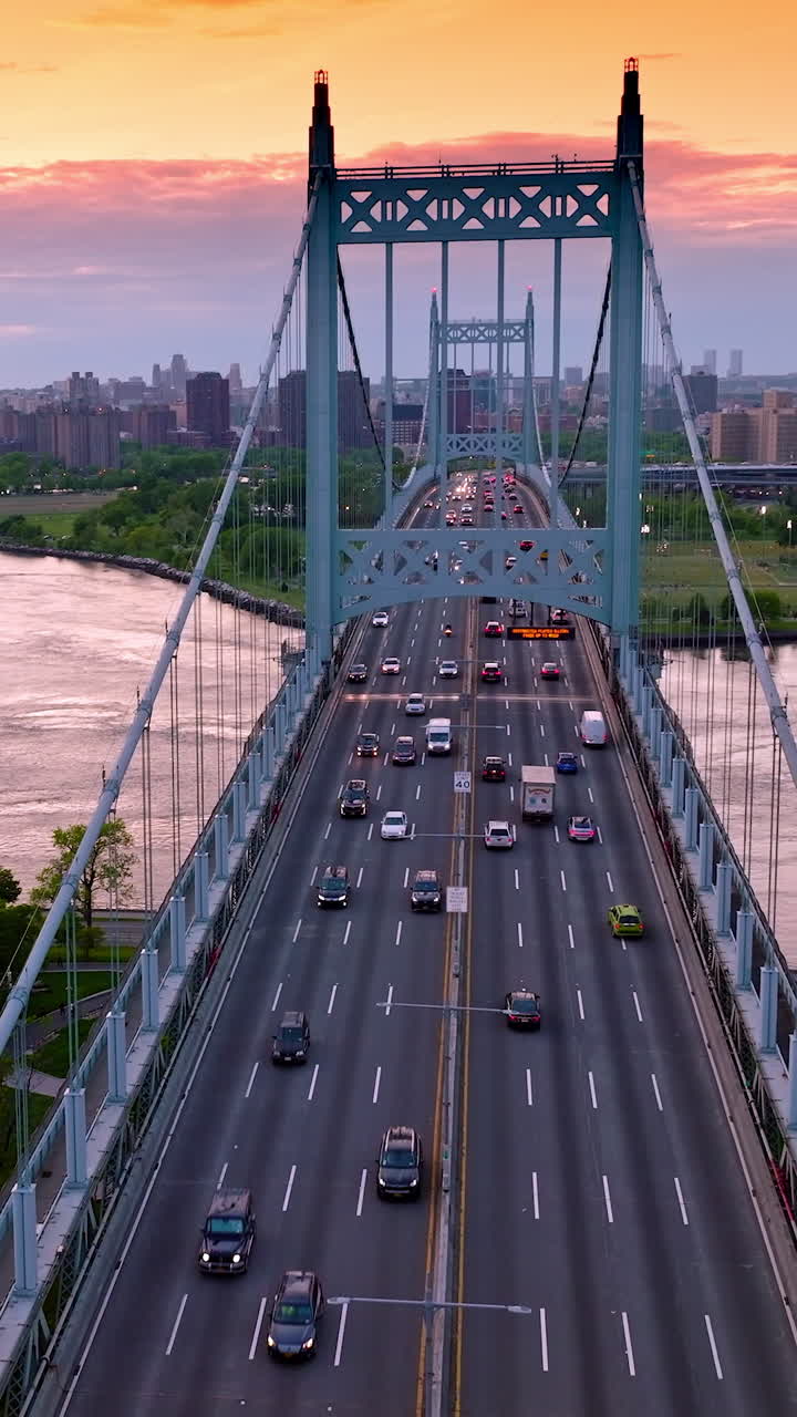 The Triborough bridge with moving cars against river and city panorama. Manhattan skyscrapers at the backdrop of orange sky. Vertical video