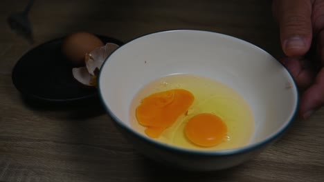 hand breaking an egg and then beats it with another already in the bowl, scrambling eggs in a bowl