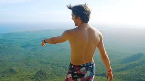 In-the-shot-you-can-see-young-shirtless-caucasian-guy-standing-on-the-top-of-a-mountain-and-looking-into-a-beautiful-Curacao-island-landscape---Christoffelberg