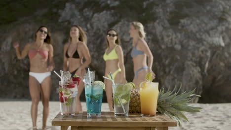 cold refreshing cocktails on table and girls dancing on beach