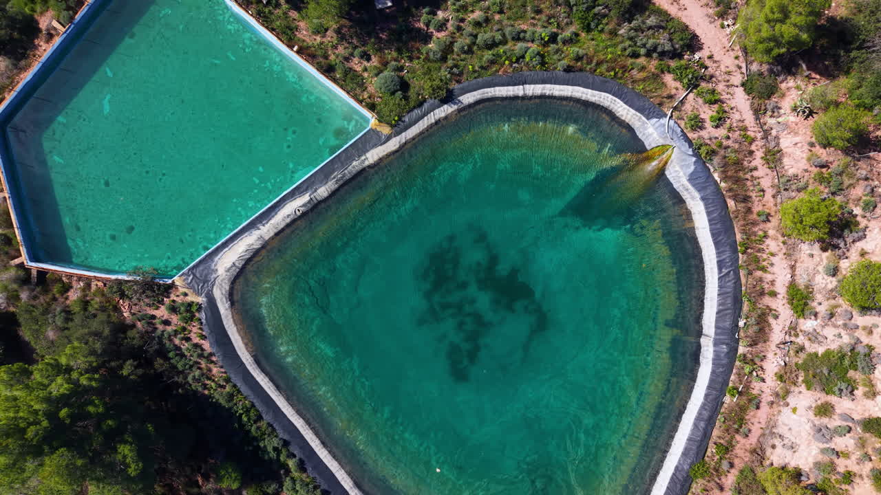 Deux réservoirs d'eau turquoise entourés d'une garrigue méditerranéenne sèche vus d'en haut.