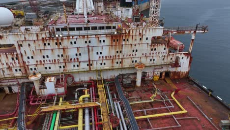 aerial drone view of an old red tanker with a heavily rusted superstructure. the aging vessel is docked and prepared for dismantling into scrap metal at an industrial shipbreaking yard.