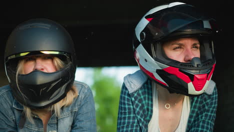 two women in helmets leaning forward, intensely focused on something off-screen, one is in a black helmet and the other in a red and white helmet