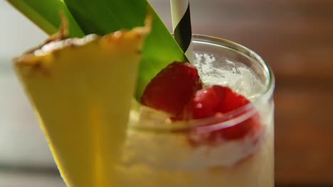 close up of pina colada cocktail on table, with raspberries and pineapple