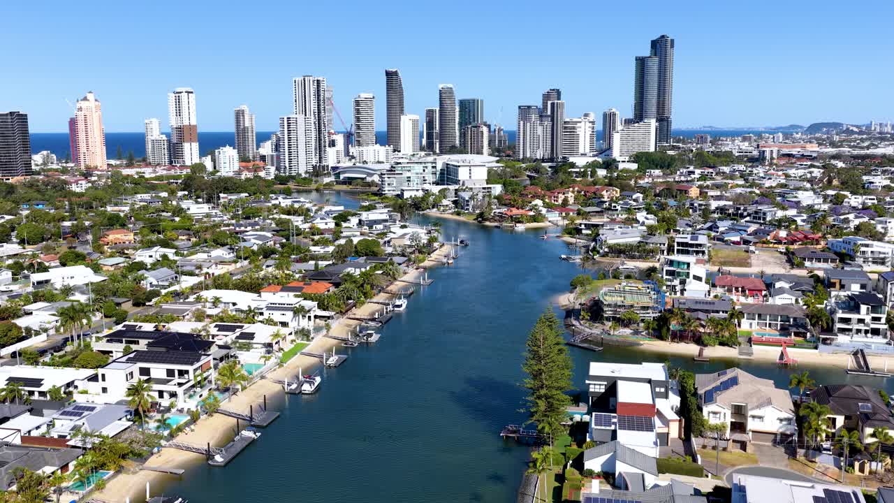 Drone glides above river, residential houses, and city skyscrapers under bright daylight, Gold Coast