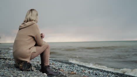 Der-Blick-Vom-Rücken-Einer-Frau,-Die-Den-Stürmischen-Himmel-über-Dem-Meer-Bewundert.-Sitzt-Am-Ufer