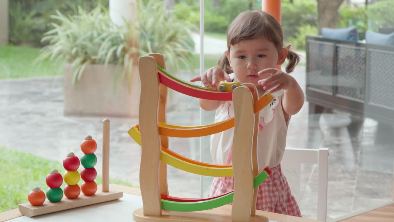 una niña pequeña juega con coches de juguete de madera y montañas rusas, experimentando con la gravedad en una sala de juegos bien iluminada