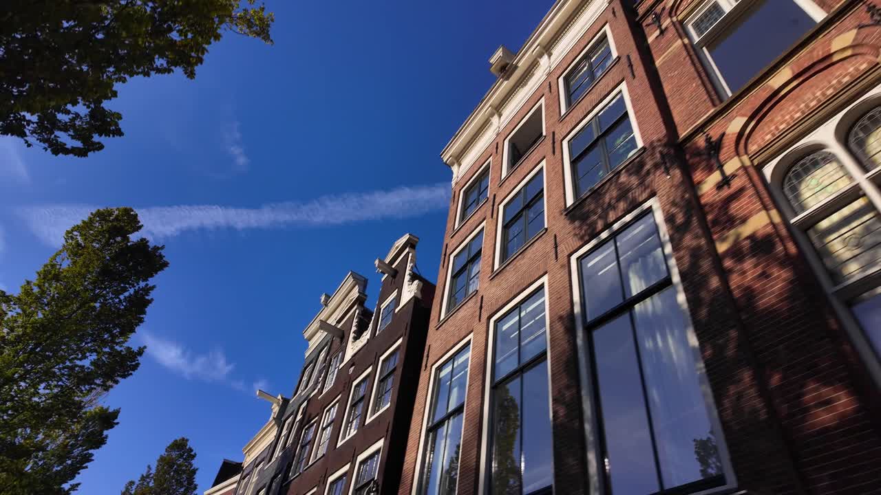 View from below of Amsterdam’s traditional gabled canal houses with bright sunlight and shadows. Location: Amsterdam, Noord-Holland, Netherlands (Amsterdam, Noord-Holland, Nederland)
