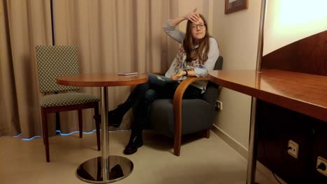 young woman with glasses, long hair, casual clothes listening to conversation, reacting with a big smile to funny comment sitting in the chair of her room