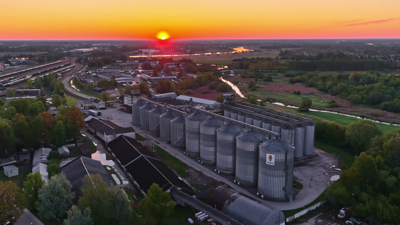 Industriesilos bei Sonnenuntergang, friedliche Kleinstadt, Fluss, Bahngleise, goldene Stunde.