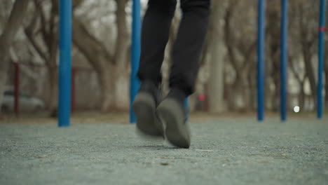 close-up of a person s legs wearing a black jeans and canvas jogging quickly, with a blurred view of a cars passing from the left across the road and blue iron bars in the background