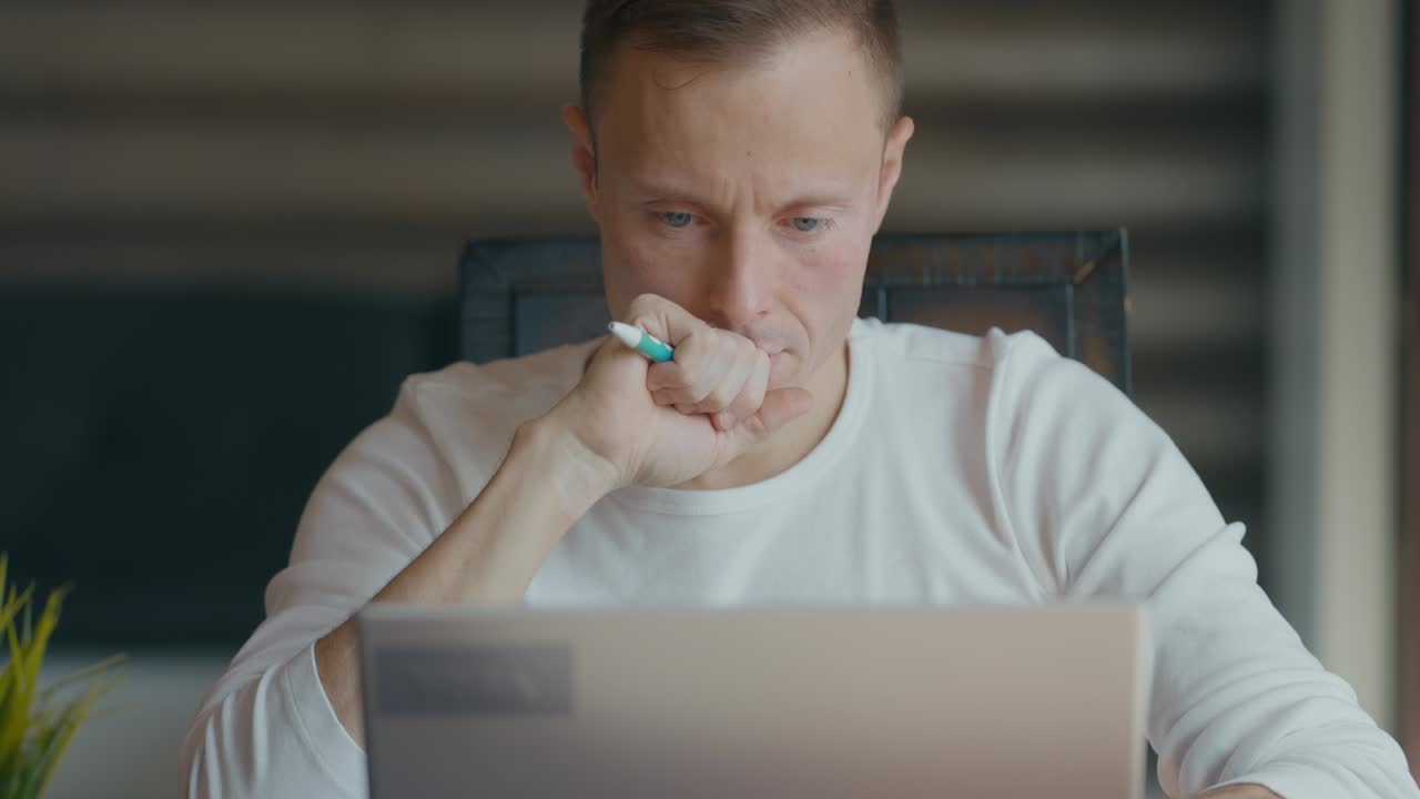 Young man is looking intently the laptop screen while sitting his desk in the room. Video