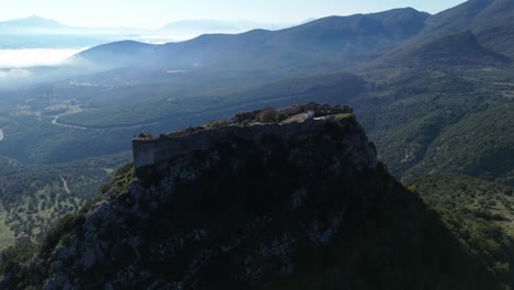 órbita panorámica aérea alrededor del castillo de karytaina con nubes bajas y brumosas en el valle de abajo en un día soleado