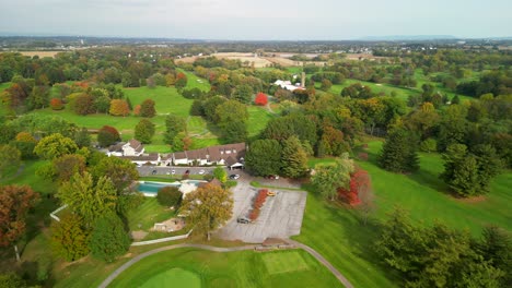 aerial drone view of country club including golf course, tennis court, and pool, during fall