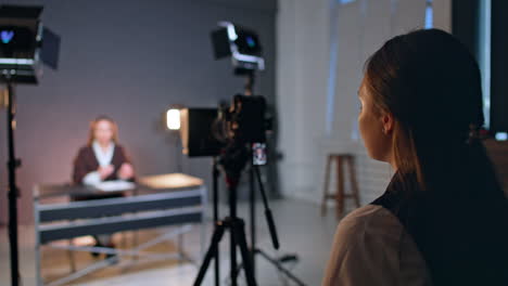 rear view of young lady standing near the camera. unrecognized female at desk talks to camera for blog content. blurred backdrop.