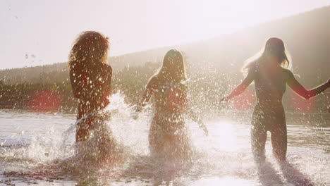 three female friends running and splashing in a lake