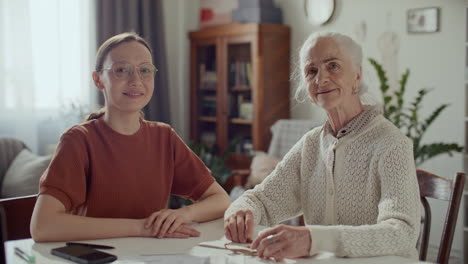 portrait of female caregiver and elderly woman sitting at table in living room