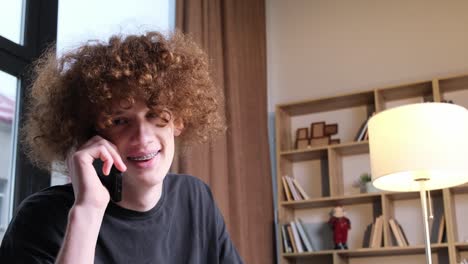 a young man with a strange hairstyle is talking on the phone a young man with a strange hairstyle is talking on the phone happy curly redhaired young man talking on the phone technologies and communications