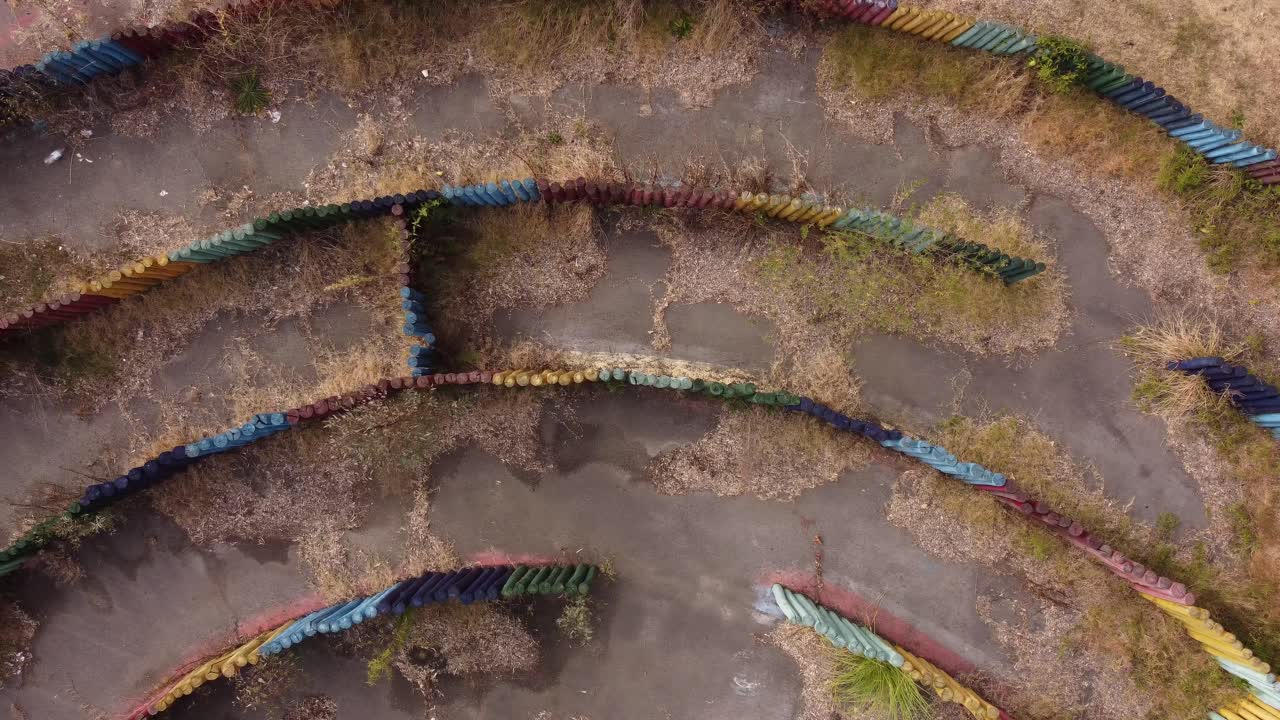 toma aérea de arriba hacia abajo de un laberinto circular vacío y cubierto de maleza en un paisaje escénico durante el día